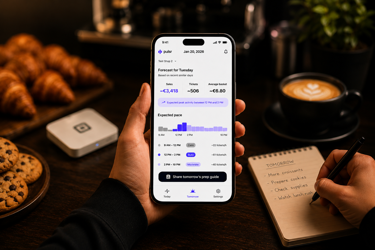 A shop owner checking tomorrow's Pulsr prep plan on their phone, next to a Square reader, fresh croissants and a latte.